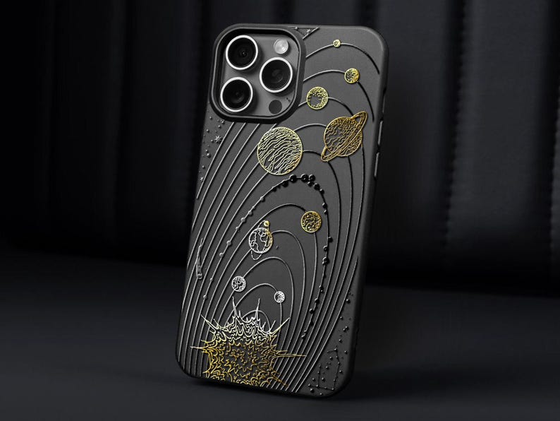 Peut inclure: Coque de t&eacute;l&eacute;phone noire avec un motif plan&eacute;taire d&eacute;taill&eacute;. L'&eacute;tui pr&eacute;sente des accents dor&eacute;s et argent&eacute;s repr&eacute;sentant des plan&egrave;tes, des &eacute;toiles et des lignes orbitales. Le motif est en relief sur l'&eacute;tui, cr&eacute;ant une surface textur&eacute;e. Les lentilles de la cam&eacute;ra sont visibles en haut.