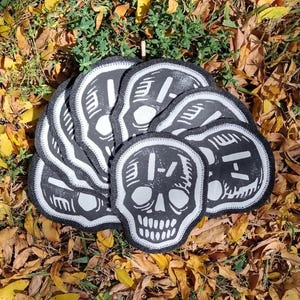 May include: A stack of black and white skull patches with a white "X" on the forehead. The patches are sewn with a white thread around the edges.