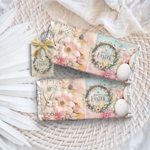 Può includere: Due involucri di barrette di cioccolato con un design floreale rosa pastello e blu. Gli involucri presentano un coniglietto, una ghirlanda con il testo "Buona Pasqua" e uova color pastello.
