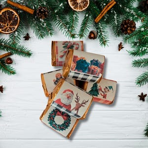May include: A collection of wrapped chocolate bars with festive Christmas designs, including Santa Claus, gifts, and elves. The bars are arranged on a white wooden surface, surrounded by pine branches, cinnamon sticks, and dried orange slices.