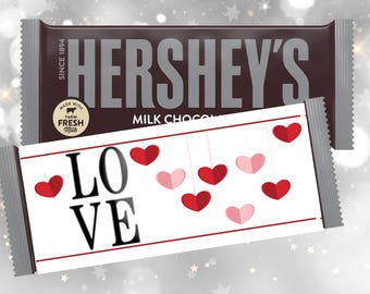 May include: Hershey's Milk Chocolate bar with a decorative wrapper featuring the word "LOVE" and hanging red and pink hearts. The Hershey's bar is dark brown with silver text and packaging.