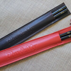 May include: Two sets of black chopsticks in leather cases. One case is red and says "Phu & My". The other case is black and says "Phu & My".