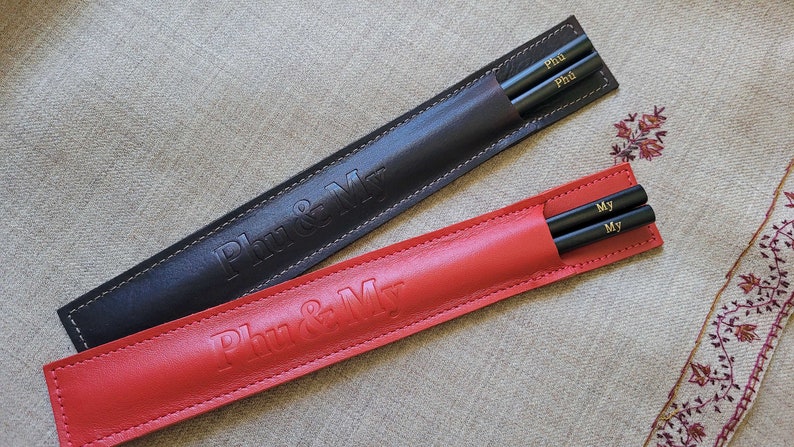 May include: Two sets of black chopsticks in leather cases. One case is red and says "Phu & My". The other case is black and says "Phu & My".