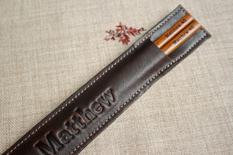 May include: A brown leather chopstick case with the name "Matthew" embossed on the front. The case contains two wooden chopsticks with the name "Matthew 40" engraved on them.