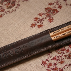 May include: A brown leather chopstick case with the name "Oliver" embossed on the front. The case contains two wooden chopsticks with the messages "For my sushi lover" and "Love, your princess" engraved on them.