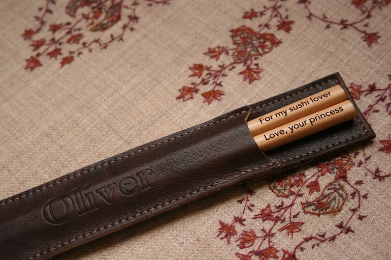 May include: A brown leather chopstick case with the name "Oliver" embossed on the front. The case contains two wooden chopsticks with the messages "For my sushi lover" and "Love, your princess" engraved on them.