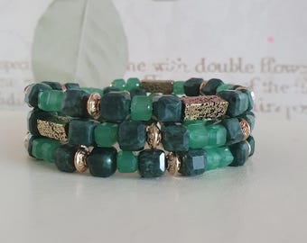 May include: Three green beaded bracelets with gold-coloured accents. The bracelets feature faceted, square-shaped beads in varying shades of green, interspersed with gold-toned spacers and rectangular decorative elements.