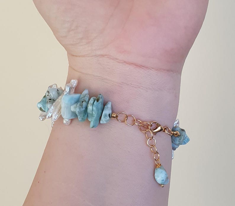 Puede incluir: Una pulsera dorada con fragmentos irregulares de piedras preciosas azul claro y acentos de perlas blancas. La pulsera se asegura con un cierre de mosquet&oacute;n y una cadena ajustable. Las piedras preciosas miden aproximadamente 1,3 cm de largo.