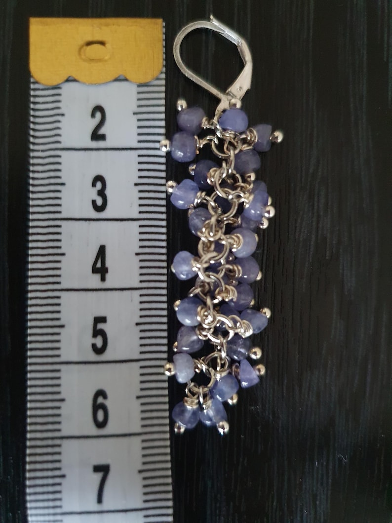 Puede incluir: Un pendiente de plata con un grupo de peque&ntilde;as cuentas de color p&uacute;rpura claro. El pendiente mide aproximadamente 6,35 cm de largo. Las cuentas est&aacute;n ensartadas con eslabones de cadena plateados, creando un efecto colgante. Cierre de palanca.