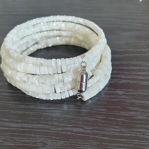 Può includere: Braccialetto bianco multifilo realizzato con piccole perle rotonde iridescenti con chiusura magnetica.
