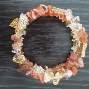 Könnte beinhalten: Ein Armband aus kleinen, unregelmäßigen Stücken von Karneol, klarem Quarz und Citrin, durchsetzt mit goldfarbenen Metallakzenten.
