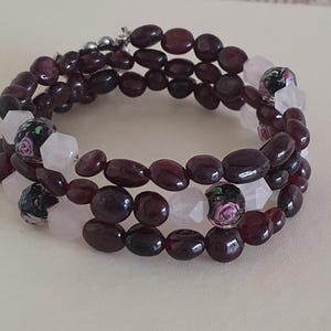 May include: A wrap-around bracelet with multiple strands of dark red oval beads, white and pink faceted beads, and decorative floral beads. The bracelet is designed to wrap around the wrist, suitable for various wrist sizes. The beads are approximately 0.5 cm in diameter.