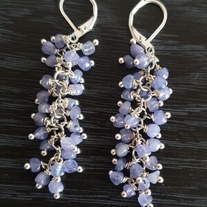Puede incluir: Un par de pendientes colgantes con racimos de peque&ntilde;as piedras preciosas de color azul claro. Los pendientes tienen cierres de palanca plateados y est&aacute;n suspendidos de una serie de delicadas cadenas plateadas. Las piedras preciosas miden aproximadamente 0,6 cm de di&aacute;metro.