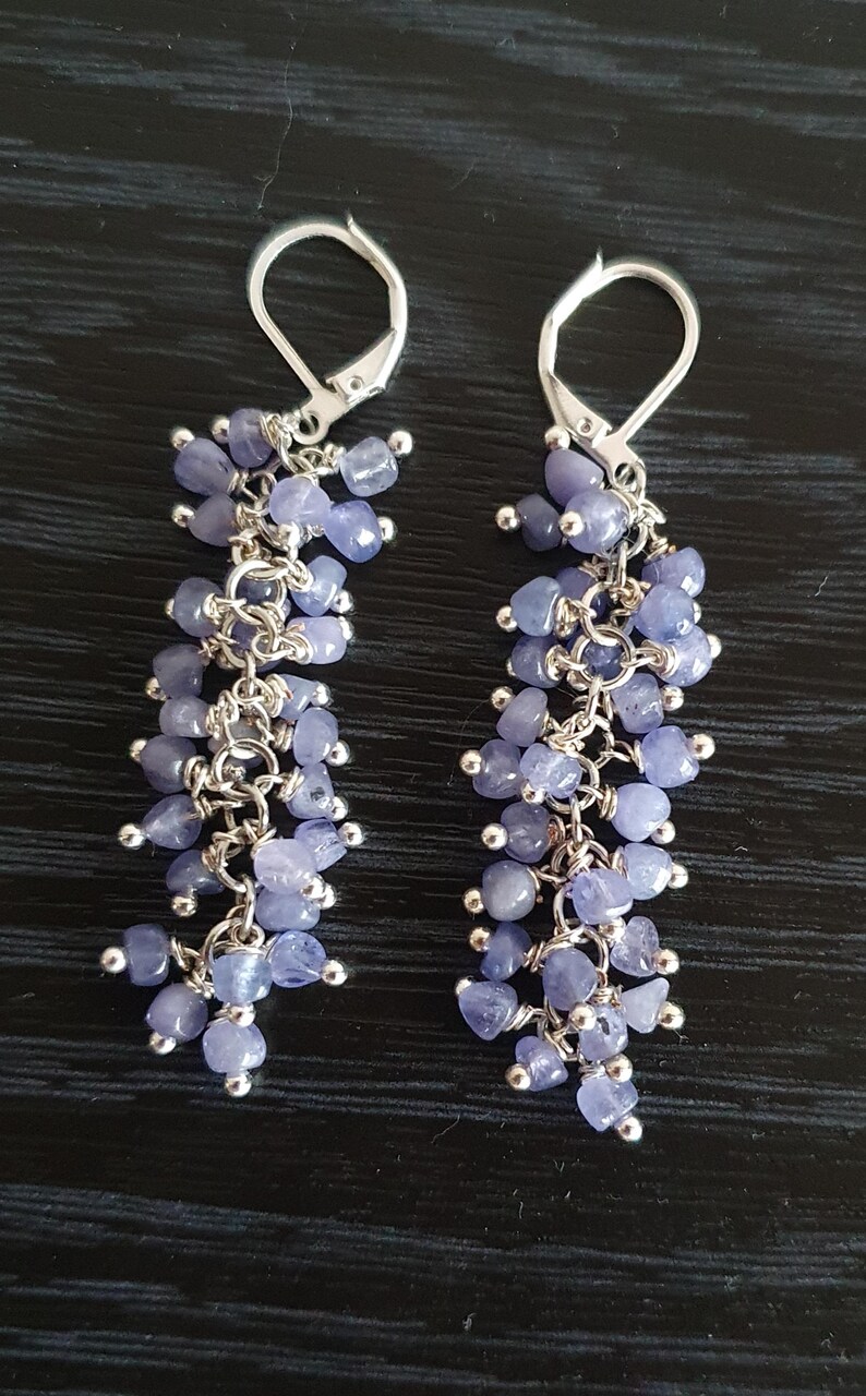 Puede incluir: Un par de pendientes colgantes con racimos de peque&ntilde;as piedras preciosas de color azul claro. Los pendientes tienen cierres de palanca plateados y est&aacute;n suspendidos de una serie de delicadas cadenas plateadas. Las piedras preciosas miden aproximadamente 0,6 cm de di&aacute;metro.