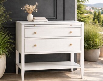 Mesita de noche blanca con cajones, acabado en alabastro, herrajes dorados, estilo moderno y lujoso.