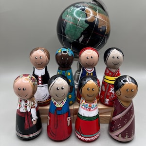 Puede incluir: Un conjunto de muñecas de madera pintadas a mano, cada una representando una cultura diferente, frente a un pequeño globo terráqueo. Las muñecas visten trajes tradicionales, con diversos colores y patrones. El globo tiene una base negra con detalles verdes y dorados.