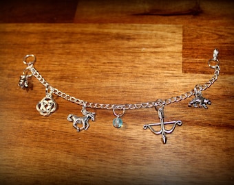 May include: Silver charm bracelet with various charms, including a horse, bear, bow and arrow, and Celtic knot. The bracelet is displayed on a wooden surface.
