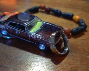 May include: A dark brown toy car with a silver ring next to it. The car has a shiny finish and a yellow interior. The ring is made of metal and has a polished finish.