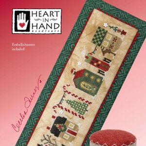 May include: A cross-stitch pattern for a Christmas village scene with the text "Christmas tiny town". The pattern features a row of houses, a Christmas tree, and candy canes.