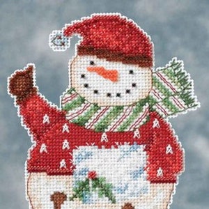 May include: A cross-stitch pattern of a snowman wearing a red jumper, green and white striped scarf, and a red hat. The snowman is holding a sprig of holly.