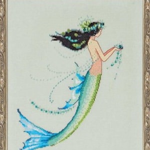 May include: Cross-stitch artwork of a mermaid with flowing black hair and a floral crown. The mermaid's tail is a gradient of blue and green, and she holds a string of beads. The artwork is framed in a gold-colored ornate frame.