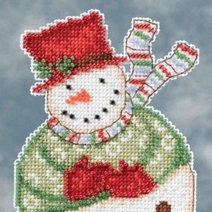 May include: A cross-stitched snowman ornament with a red top hat, scarf, and mittens. The snowman has a carrot nose, black dot eyes, and a green sweater. The ornament is round with a bell at the bottom.