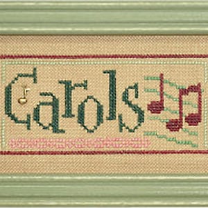 May include: A framed cross-stitch design with the word "Carols" in green letters and musical notes in red and green. The design is on a beige background and is framed in a light green frame.