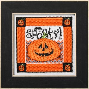 May include: A cross-stitch design featuring a smiling jack-o'-lantern pumpkin with the word "Spooky!" above it. The design is framed in black and has a white background.