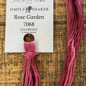 May include: A skein of pink embroidery floss with a tag that reads "Rose Garden" from "Simply Shaker" and "The Gentle Art." The floss is a vibrant shade of pink, with a colorfast label.
