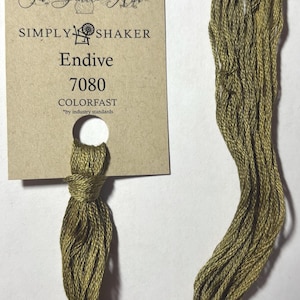 May include: A skein of olive green embroidery floss with a tag. The tag reads "The Gentle Art SIMPLY SHAKER Endive 7080 COLORFAST." The floss is tied at the bottom and hangs down in a loose loop.