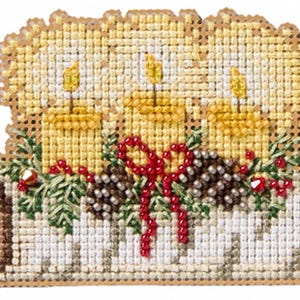 May include: A cross-stitch embroidery piece featuring three yellow candles with lit flames, arranged on a white textured base. The design includes green pine needles, brown pinecones, and red beaded accents, all stitched onto a perforated board.