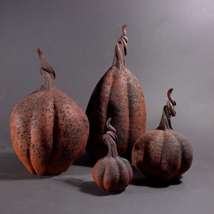 May include: Four ceramic pumpkins of varying sizes, all with a speckled brown and black glaze. The pumpkins have a rustic, handmade appearance.