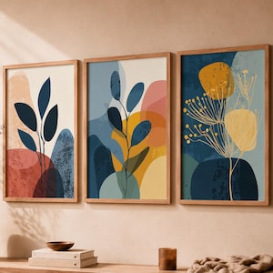 Peut inclure: Trois impressions d'art mural rectangulaires dans des cadres en bois clair présentant des illustrations botaniques abstraites avec des feuilles bleu foncé, des formes florales jaunes et des blocs de couleurs géométriques superposés.