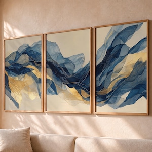 Könnte beinhalten: Ein dreiteiliges Wandbild-Set bestehend aus drei gerahmten rechteckigen Drucken. Jeder Druck zeigt abstrakte, fließende Linien in den Farben Dunkelmarineblau, Hellblau und Metallic-Gold auf einem cremefarbenen Hintergrund.
