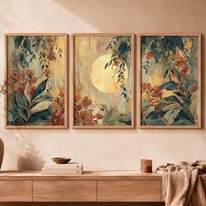 May include: A set of three rectangular wall art prints in light wood frames. The artwork features a central yellow moon surrounded by dark green foliage and orange flowers against a muted, textured background with vertical brushstroke patterns.