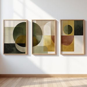 Può includere: Set di tre stampe artistiche astratte incorniciate. Ogni stampa presenta forme geometriche in tonalità di verde, marrone e oro. L'opera d'arte è esposta in una stanza ben illuminata con pavimento in legno, creando un'estetica moderna ed elegante.