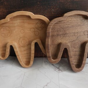 May include: Two wooden Nintendo 64 controller shaped dishes. One is made of light wood and the other is made of dark wood.
