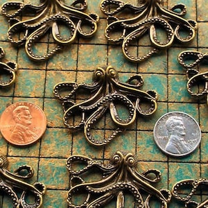 May include: Eight antique gold-toned octopus charms with detailed tentacles. The charms are arranged on a green and white checkered surface.