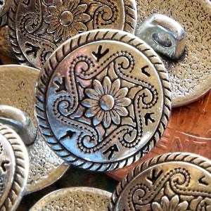 May include: A collection of silver-toned metal buttons with intricate floral designs. The buttons have a raised, textured surface and a circular shape.