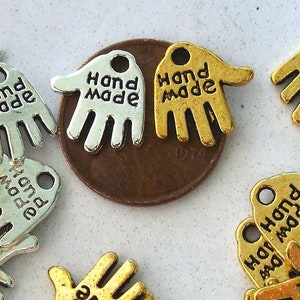 May include: A collection of silver and gold hand-shaped charms with the words "Hand Made" engraved on them.