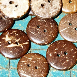 May include: A collection of round, natural coconut shell buttons. The buttons vary in shades of brown, from light tan to dark chocolate, with two holes for sewing. The buttons have a textured surface and a rustic appearance, suitable for various sewing projects.