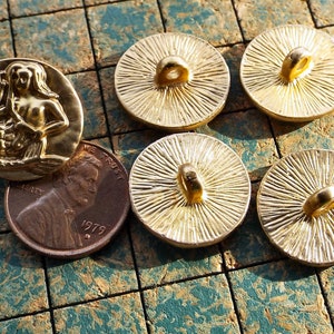 May include: Five gold-toned buttons with a mermaid design and a sunburst design. The mermaid button features a raised design of a mermaid with a tail and long hair. The sunburst buttons have a raised design of a sunburst with a loop at the top.