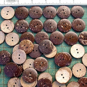 May include: A collection of brown coconut shell buttons with three holes each. The buttons are arranged in a grid pattern on a green surface.