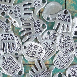 May include: Silver charm pendants with the text "Made with Love" and "Hand Made" in a variety of hand shapes.