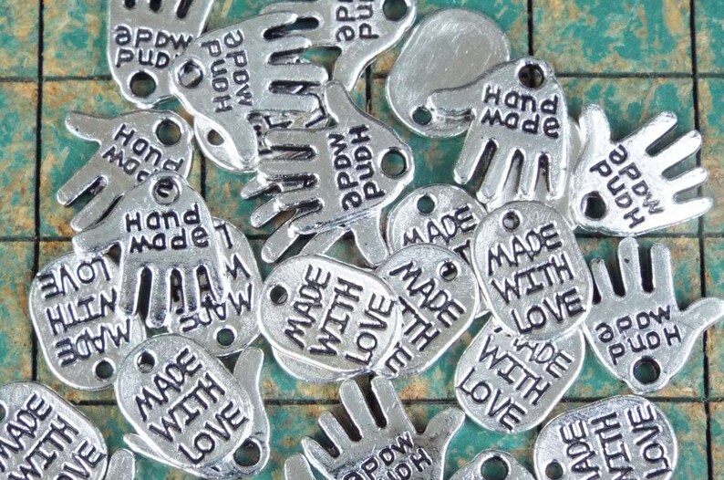 May include: Silver charm pendants with the text "Made with Love" and "Hand Made" in a variety of hand shapes.