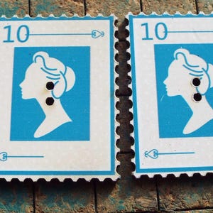 May include: Two vintage postage stamps with a blue and white design. Each stamp features a profile of a woman's silhouette, the number "10", and decorative elements. The stamps are on a textured, weathered surface.