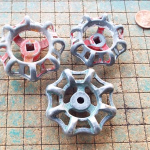 May include: Three vintage water valve handles with a starburst design. The handles are made of metal and have a silver finish with red and green accents. A penny is next to the handles for size comparison.