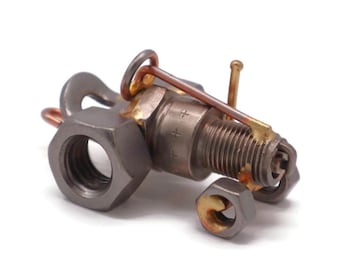 Könnte beinhalten: Eine kleine, handgefertigte Traktorskulptur aus Metallmuttern, Schrauben und einer Zündkerze. Der Traktor hat einen Kupferdraht als Griff und eine Mutter als Rad.