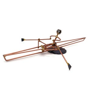 May include: A copper wire sculpture of a person rowing a boat. The boat is made of wire and has a black base. The person is sitting in the boat and holding oars.
