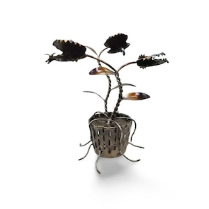 Puede incluir: Escultura metálica artesanal de una planta en maceta. La planta presenta tallos retorcidos, hojas detalladas y una maceta en forma de cesta con raíces estilizadas. La escultura es de metal oscuro con detalles en marrón y bronce.